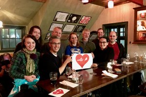 A diverse group of individuals gathered around a table, holding a sign with the Caktus Group and Wagtail CMS logo in a heart shape